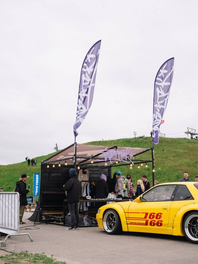 Anteater booth with brand flags and a yellow drift car parked beside it