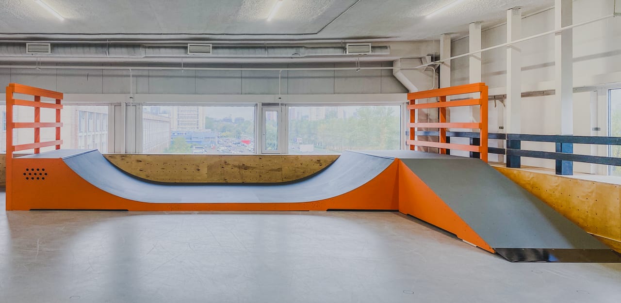 Orange and grey indoor mini ramp with a bank extension in a bright skate hall