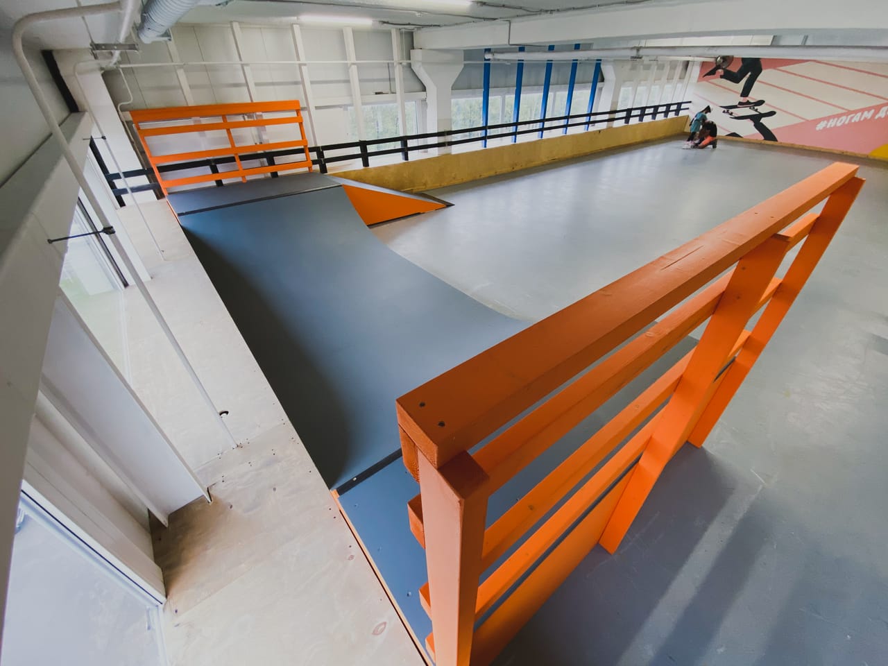 Deck and bank of the indoor mini ramp with riders in the hall behind