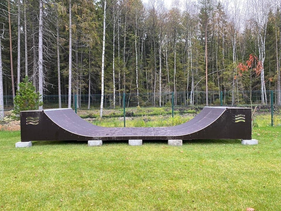 Finished black mini ramp on a lawn at the edge of a pine forest