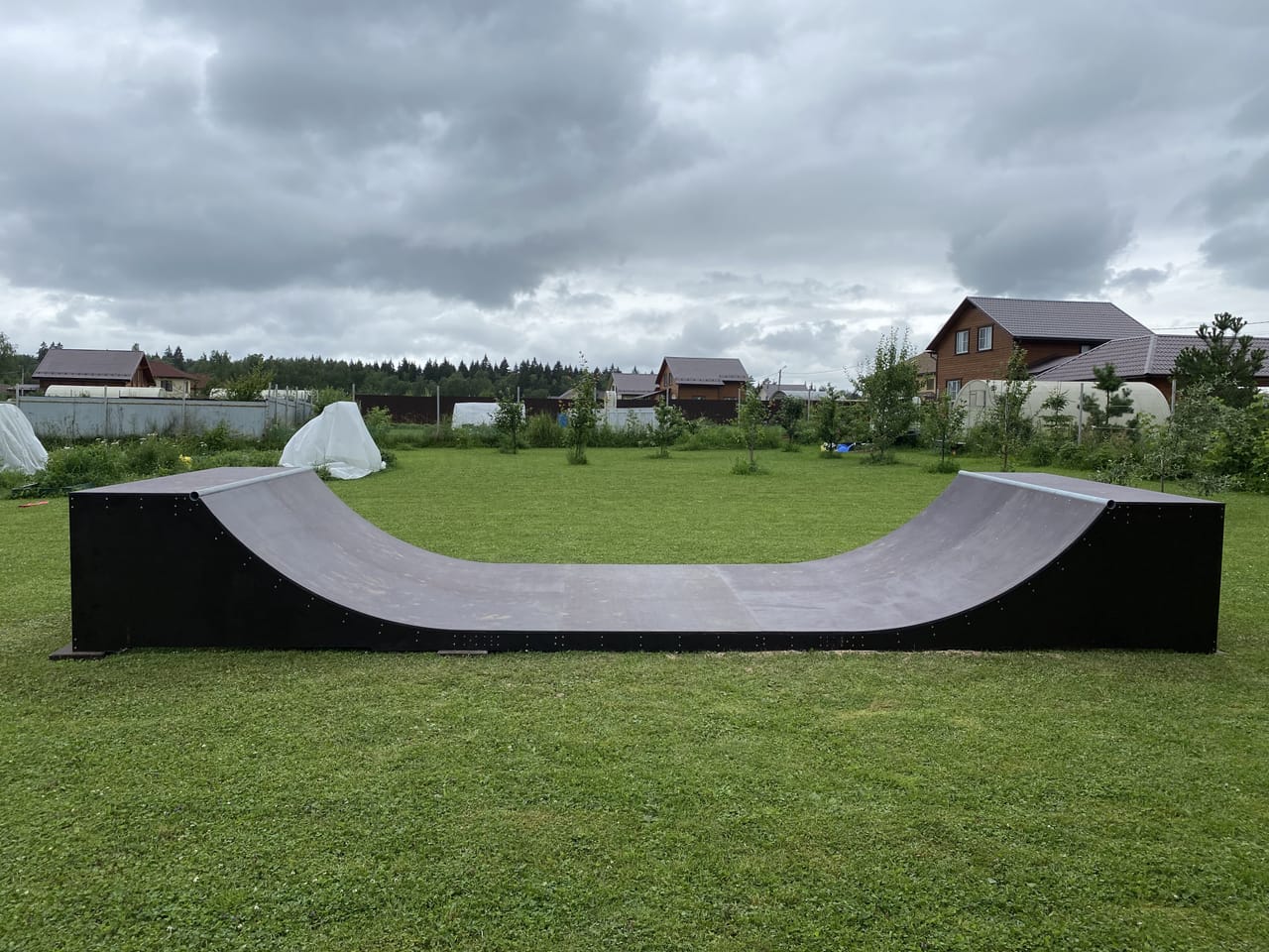 Black mini ramp with a grey riding surface on a lawn in front of country houses