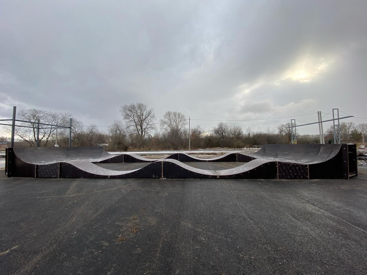 Salavat skatepark: a pump track of dark wooden rollers between two quarter pipes