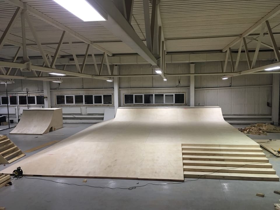 Wooden ramps and a funbox going up inside a sports hall
